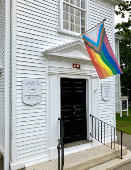 Progress Pride Flag flying over the front door of a white clapboard New England Meeting House