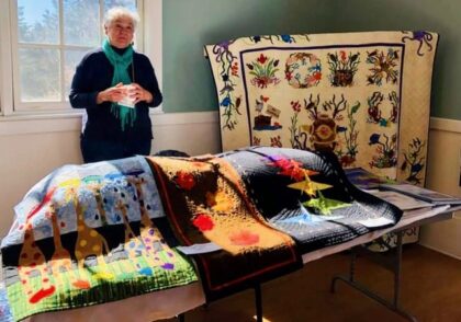 A table featuring four different quilt patterns with the quilter standing in the background holding a white ceramic cup (of coffee).