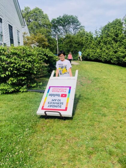 Child dragging a sign across the lawn to advertise lobster roll event.