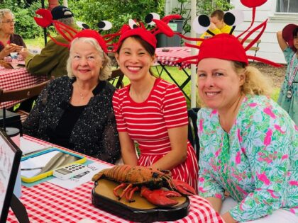 Three volunteers wearing lobster headgear sitting at a red and white checkered table selling lobster rolls.