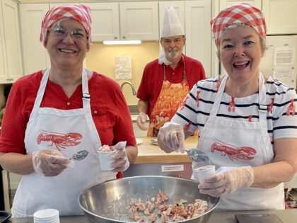 Three people shown cutting lobster meat and filling cups to measure quantity for lobster rolls.