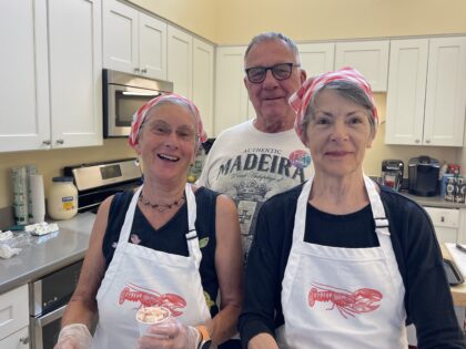 Three people (two with white and red lobster aprons) shown in kitchen during food preparation.
