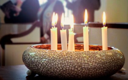 Close-up of candles burning, with people standing behind them.