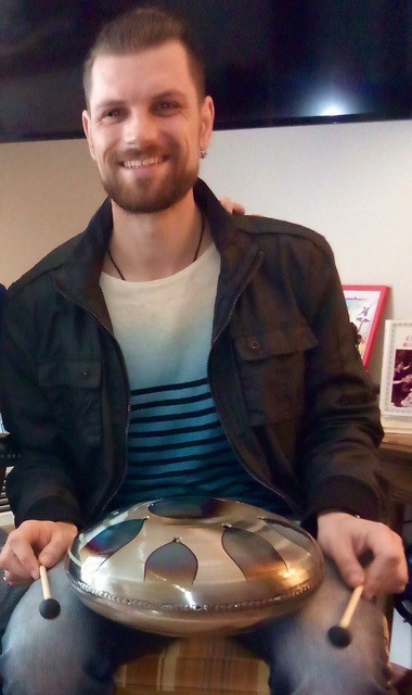 Bearded male in 20s holding gold tongue drum.